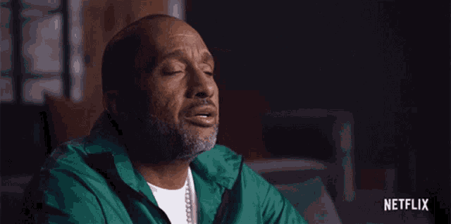 a man in a green jacket is sitting with his eyes closed and a netflix logo behind him