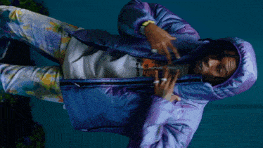 a man wearing a purple jacket and tie dye pants is laying down