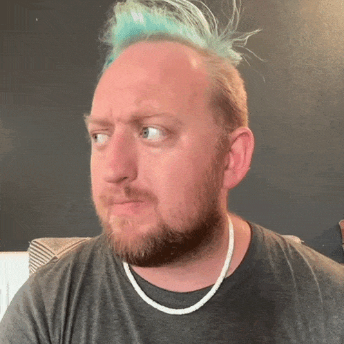 a man with a beard and blue hair is wearing a grey shirt