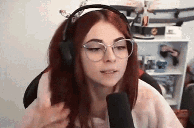 a girl with red hair is wearing headphones and glasses while talking into a microphone .