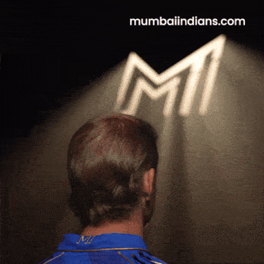 a man in a blue shirt is looking at a mumbai indians logo