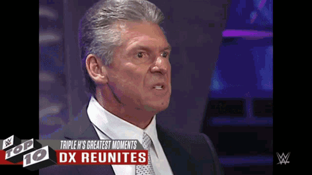 a man in a suit and tie is sitting in front of a screen that says triple h 's greatest moments