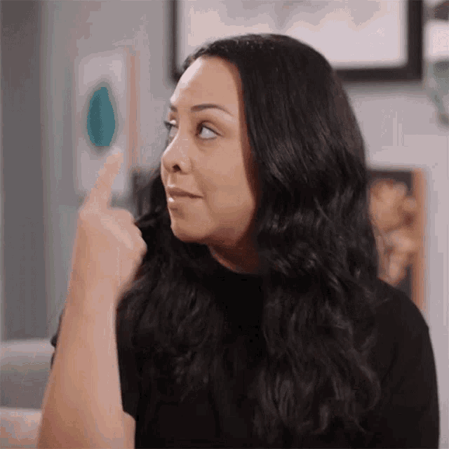 a woman with long black hair is making a funny face and pointing at something .
