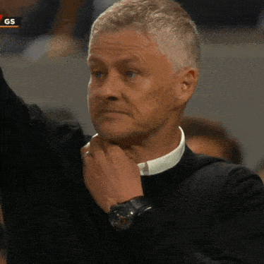 a man wearing a watch holds his hand to his chin in front of a gs banner