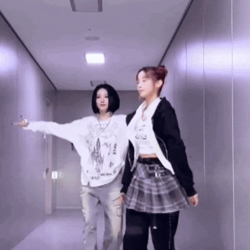 two women are dancing in a hallway and one is pointing at the camera .