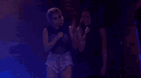 two women are singing into microphones on a stage .