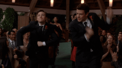 two men in suits are dancing in front of a crowd at a wedding