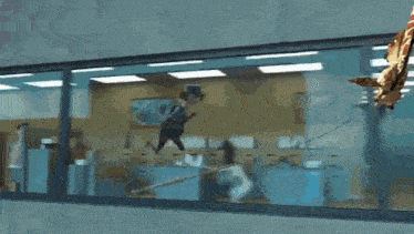 a giraffe is hanging from the ceiling of an office building while a woman tries to catch it .