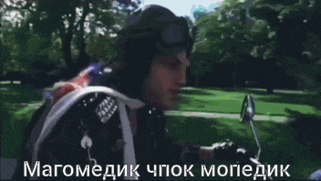 a man wearing a helmet and goggles is sitting on a motorcycle in a park ..