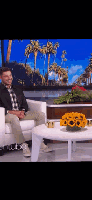 a man is sitting in a chair next to a table with sunflowers on it