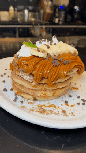 a stack of pancakes with bananas whipped cream caramel sauce and chocolate chips on a white plate