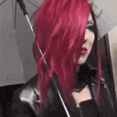 a woman with red hair is holding an umbrella and wearing a black jacket .