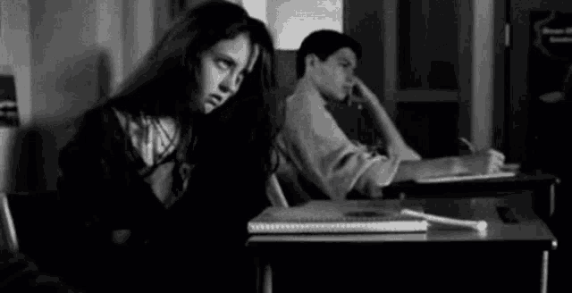 a man and a woman are sitting at a desk in a classroom .