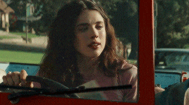 a woman is driving a red car and looking out of the window