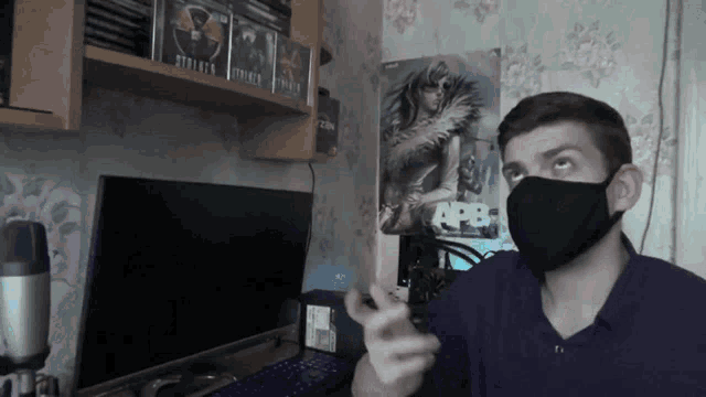 a man wearing a black mask points at something in front of a computer