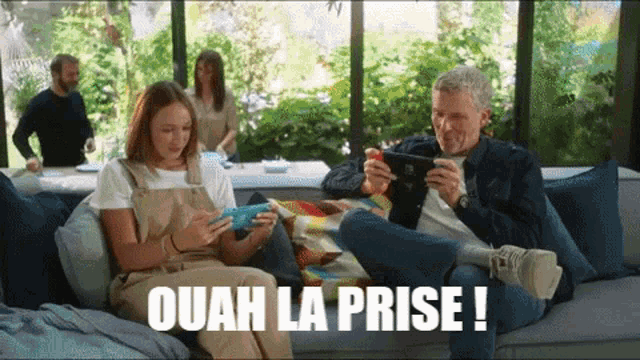 a man and a woman sitting on a couch playing a video game with the caption ouah la prise !