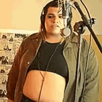 a woman is standing in front of a microphone wearing headphones and a crop top