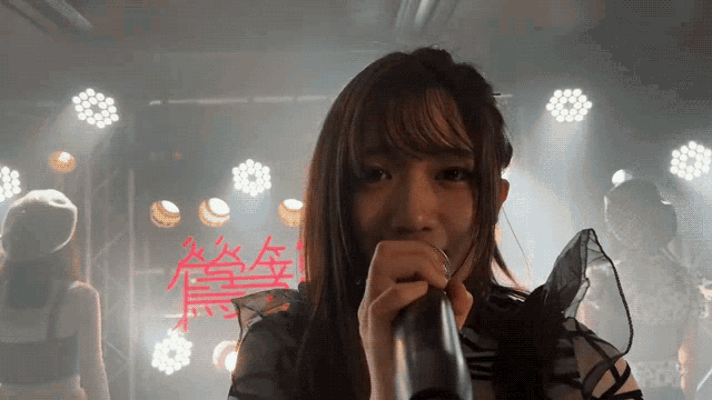 a girl is singing into a microphone with chinese writing on the wall behind her