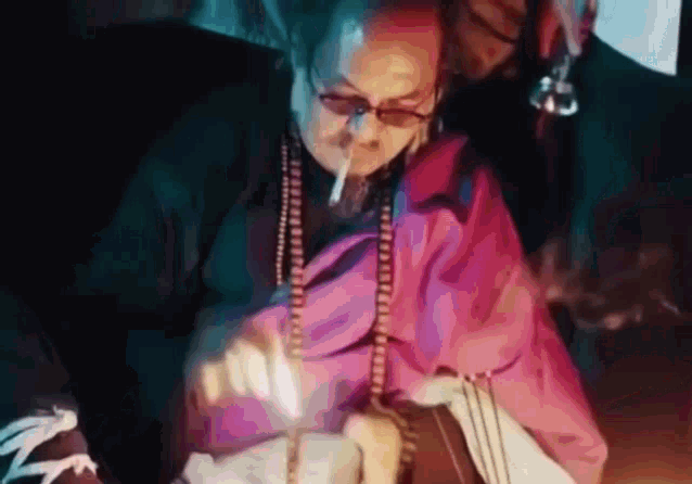 a man is smoking a cigarette in a dark room while wearing glasses .