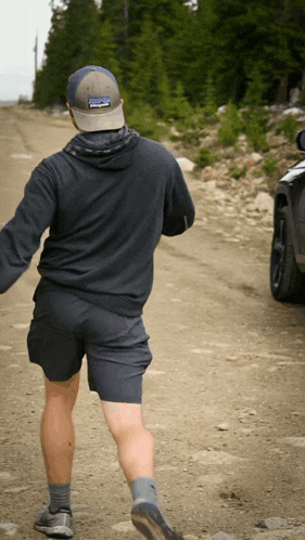 a man wearing a patagonia hat walks down a gravel road