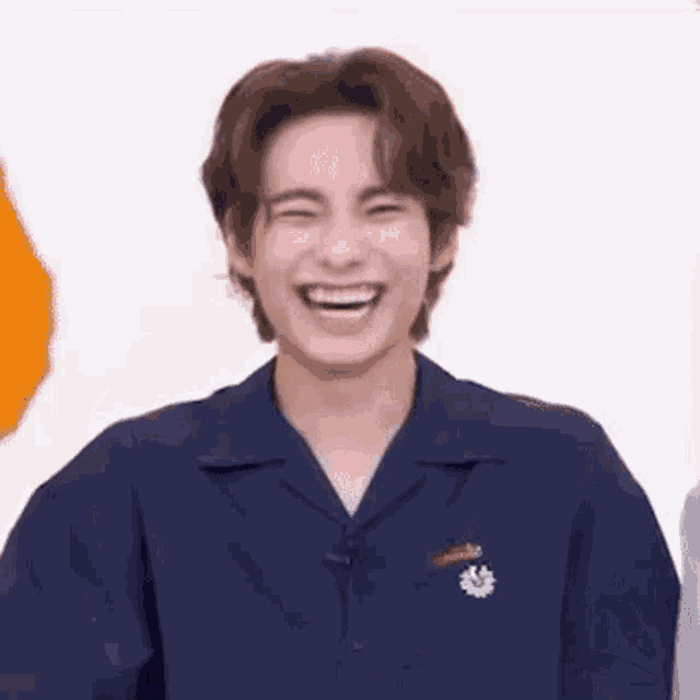 a young man in a blue shirt is laughing while standing in front of a white background .