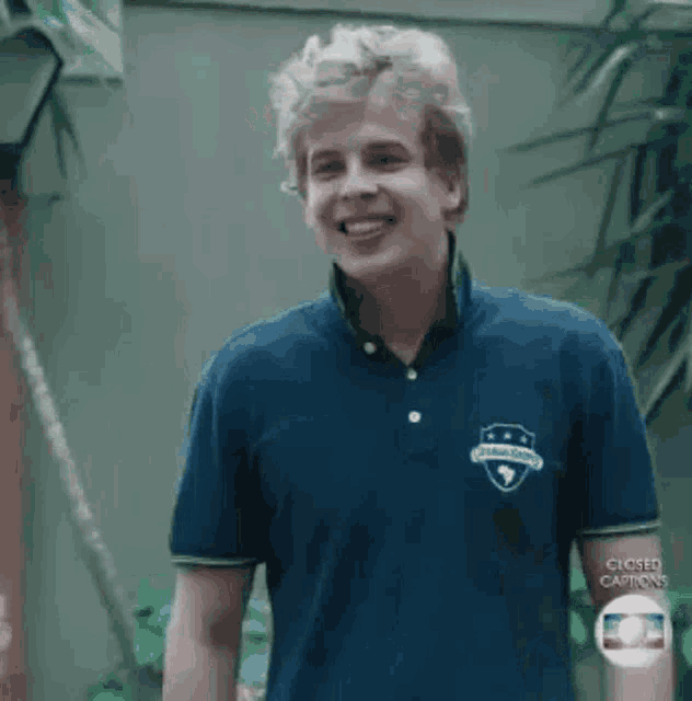 a young man wearing a blue polo shirt is smiling while standing in front of a palm tree .