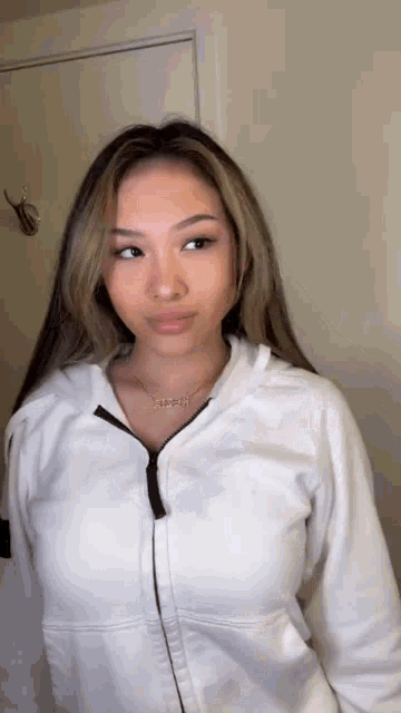 a woman is wearing a white hoodie and a necklace .