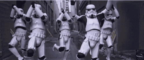a group of stormtroopers are jumping in the air in a street .