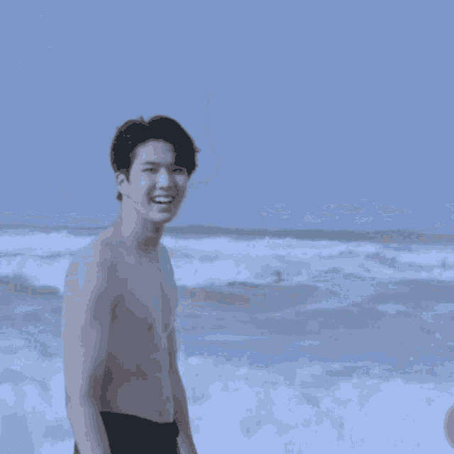a shirtless man is standing on a beach looking at the camera