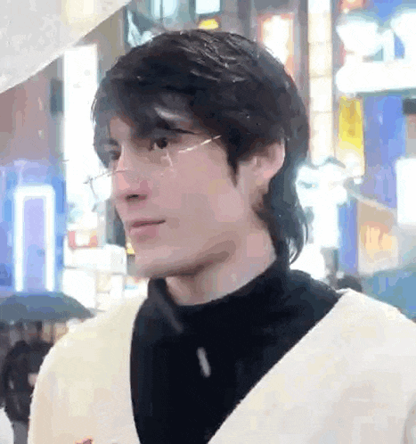 a young man wearing glasses and a black turtleneck is standing in a city street .