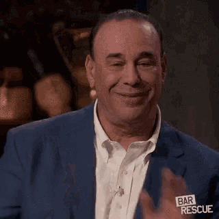 a man in a suit is smiling and clapping his hands .