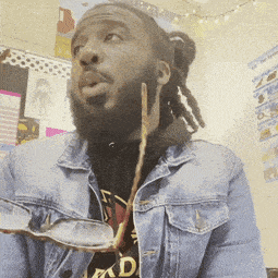 a man with dreadlocks is wearing a denim jacket and holding a pair of glasses