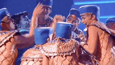a group of people dressed in gold and blue costumes are holding blue buckets on a stage .