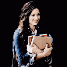 a woman is holding a stack of books and smiling .