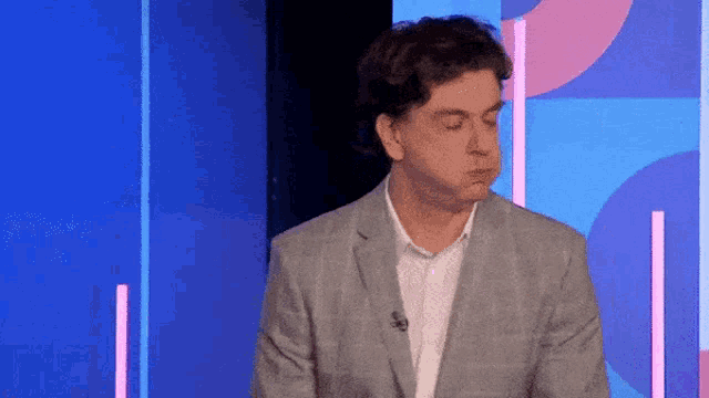 a man in a suit is standing in front of a blue and pink background