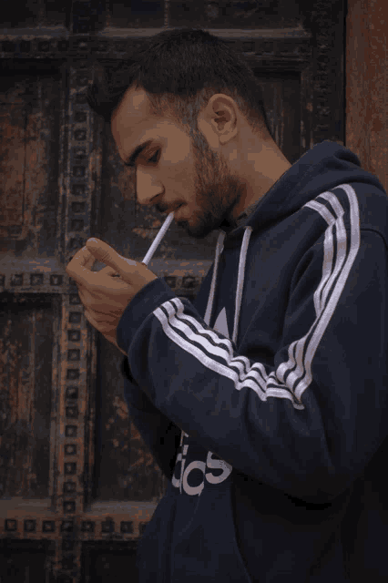 a man smoking a cigarette wearing an adidas hoodie