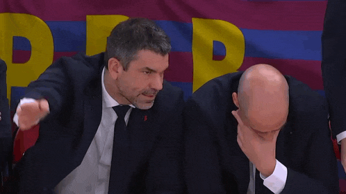two men in suits and ties are sitting in front of a barcelona flag