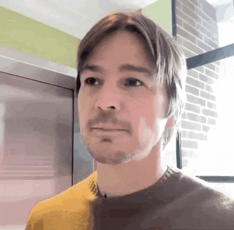 a man with a beard is wearing a yellow shirt and a brown sweater .
