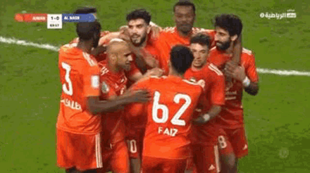a group of soccer players are hugging each other on a field . one of the players has the number 62 on his shirt .