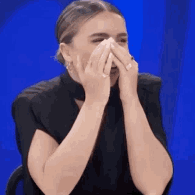 a woman is covering her mouth with her hands and laughing .