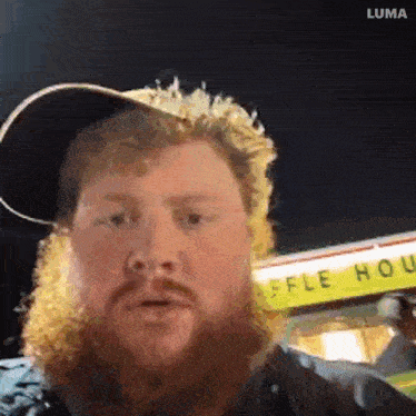 a man with a beard wearing a hat is standing in front of a food truck .