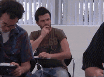 a man in a 68 shirt is sitting in a classroom with other people .