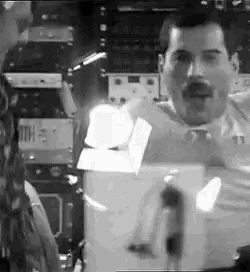 a black and white photo of a man with a mustache standing in front of a microphone in a room .