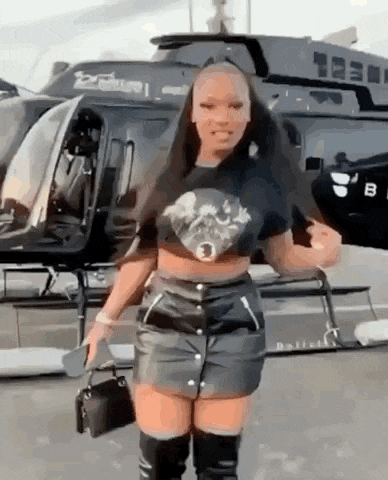 a woman is standing in front of a helicopter wearing a leather skirt and knee high boots .