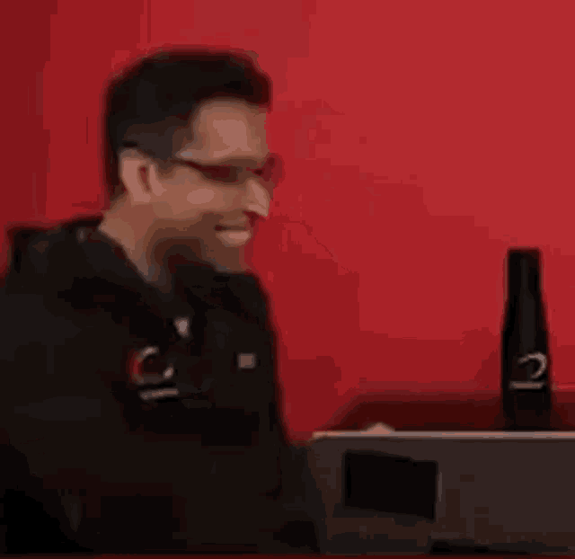 a man wearing glasses is smiling while sitting in front of a computer .
