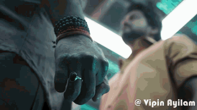 a man with a ring on his finger is holding another man 's hand with a caption that says vipin ayilam