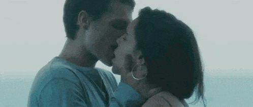 a man and a woman are kissing each other in front of the ocean .