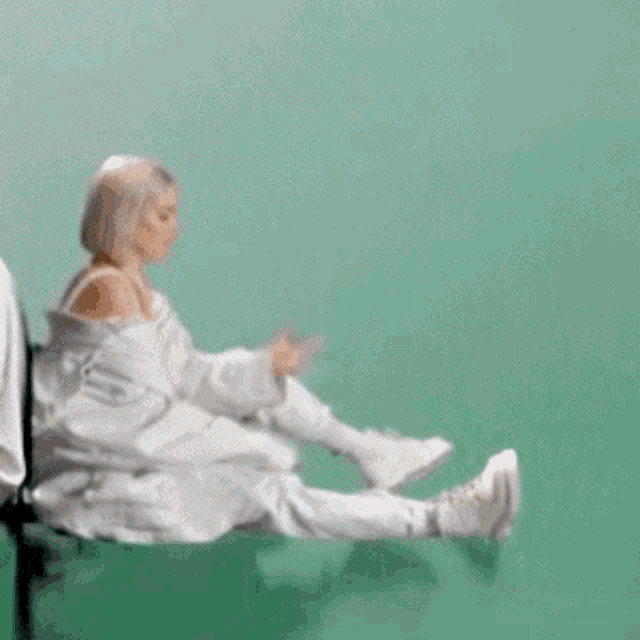 a woman in a white jumpsuit is sitting on a green surface with her legs crossed