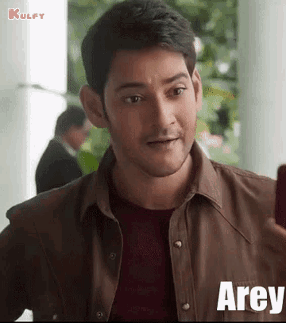 a man in a brown shirt is looking at a cell phone and the word arey is on the bottom
