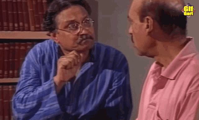 a man in a pink shirt talks to another man in a library